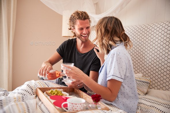 Millennial white couple celebrating with champagne, breakfast and gifts in bed, close up Высокооплачиваемая вакансия